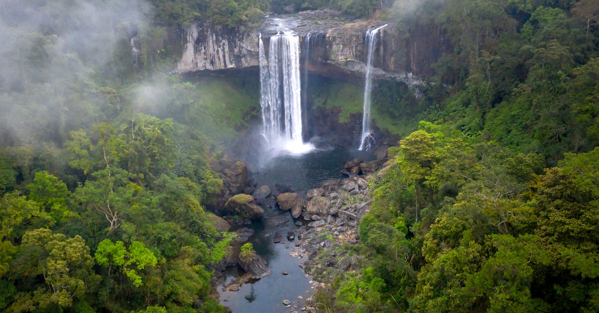 A stunning aerial view of a cascading waterfall surrounded by lush greenery in a tranquil forest setting.
