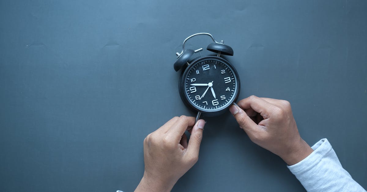 Hands adjusting a classic black alarm clock on a blue background with ample copy space.