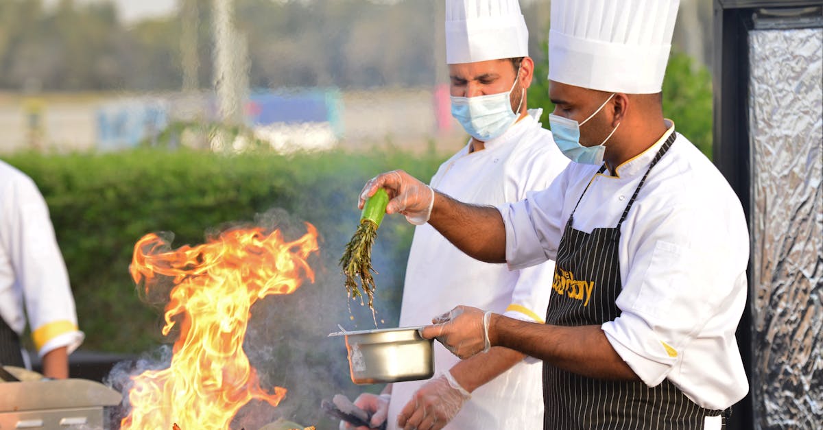 Chefs in masks grilling food with a flame outdoors, adding herbs for flavor.