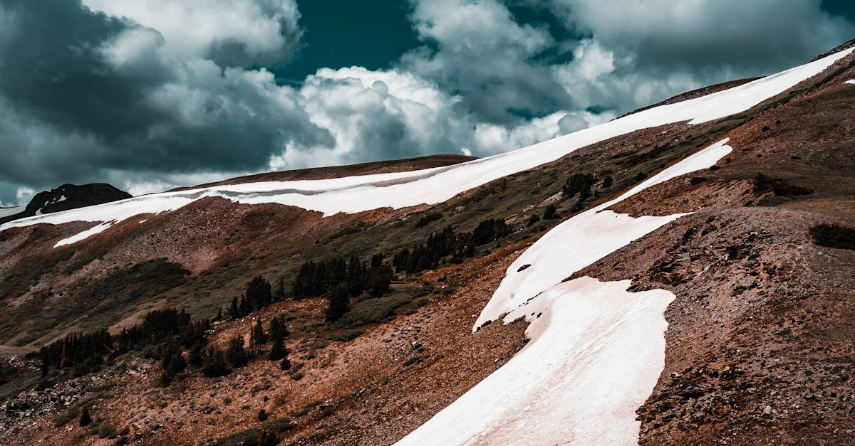 A stunning mountain scene featuring snow patches under a dynamic cloudy sky, capturing nature's beauty.