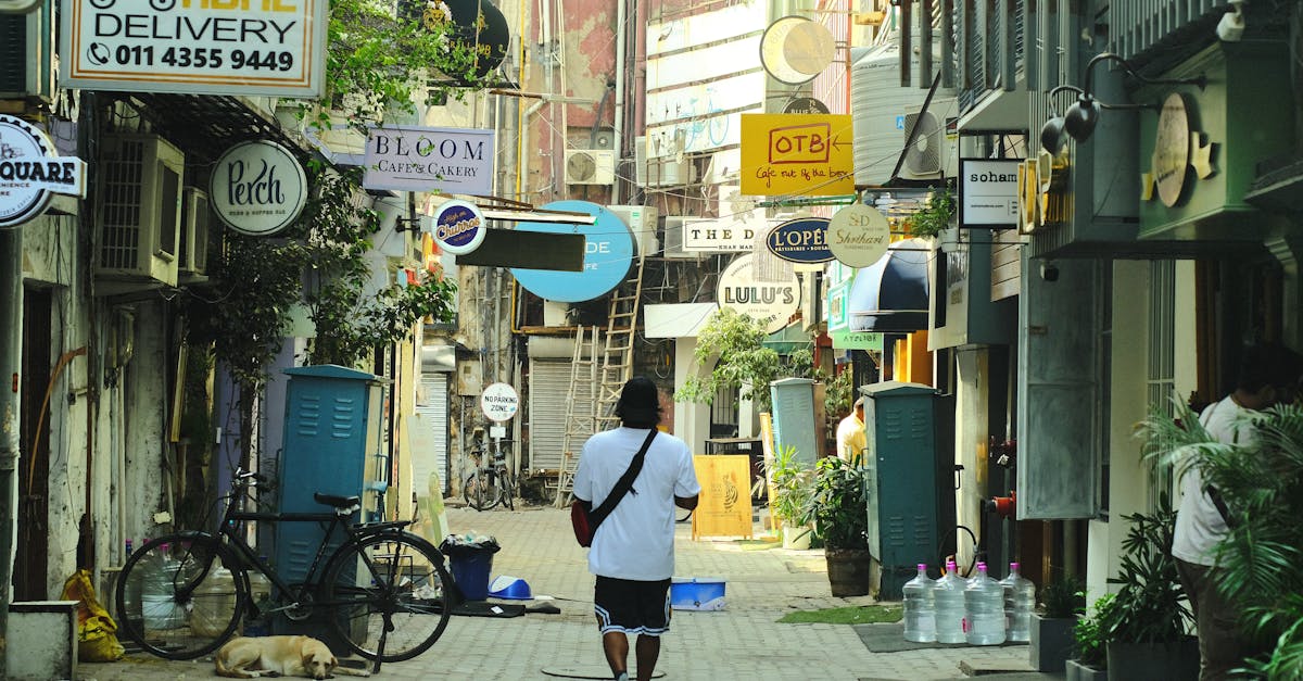 Man walking along a vibrant street with shop signs, bicycle, and resting dog.