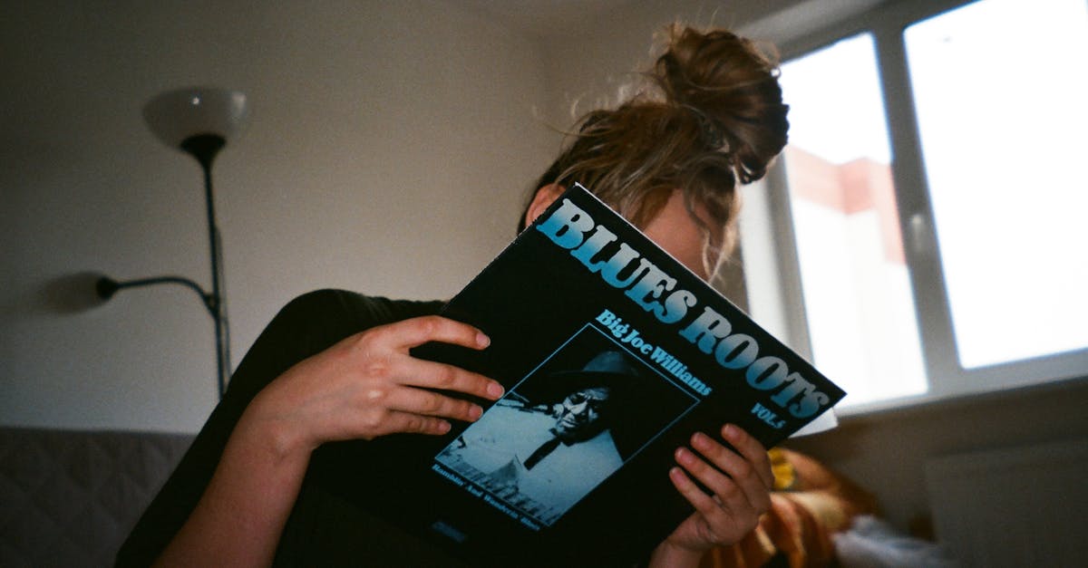 A woman holding a vintage vinyl record indoors beside a window.