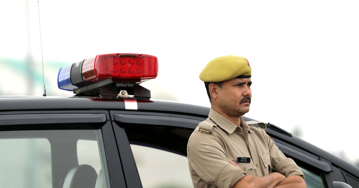Police officer standing with arms crossed beside a patrol car during the day.