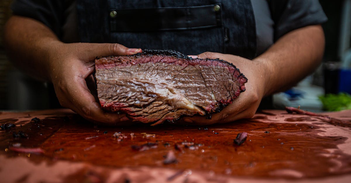 Close-up of a chef's hands holding a tender and juicy smoked brisket on a wooden board.