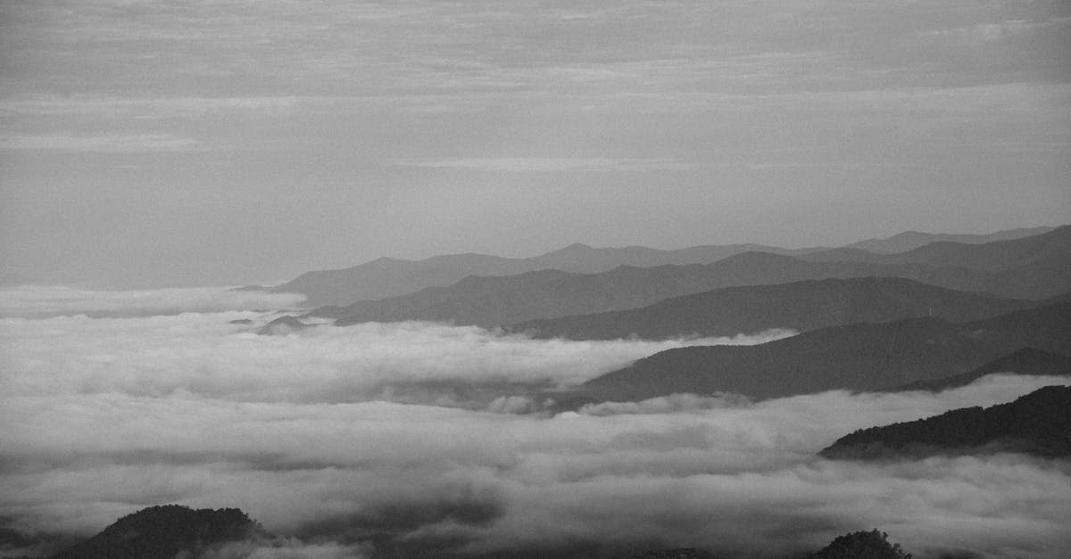 A tranquil black and white landscape view of fog rolling over the mountains.
