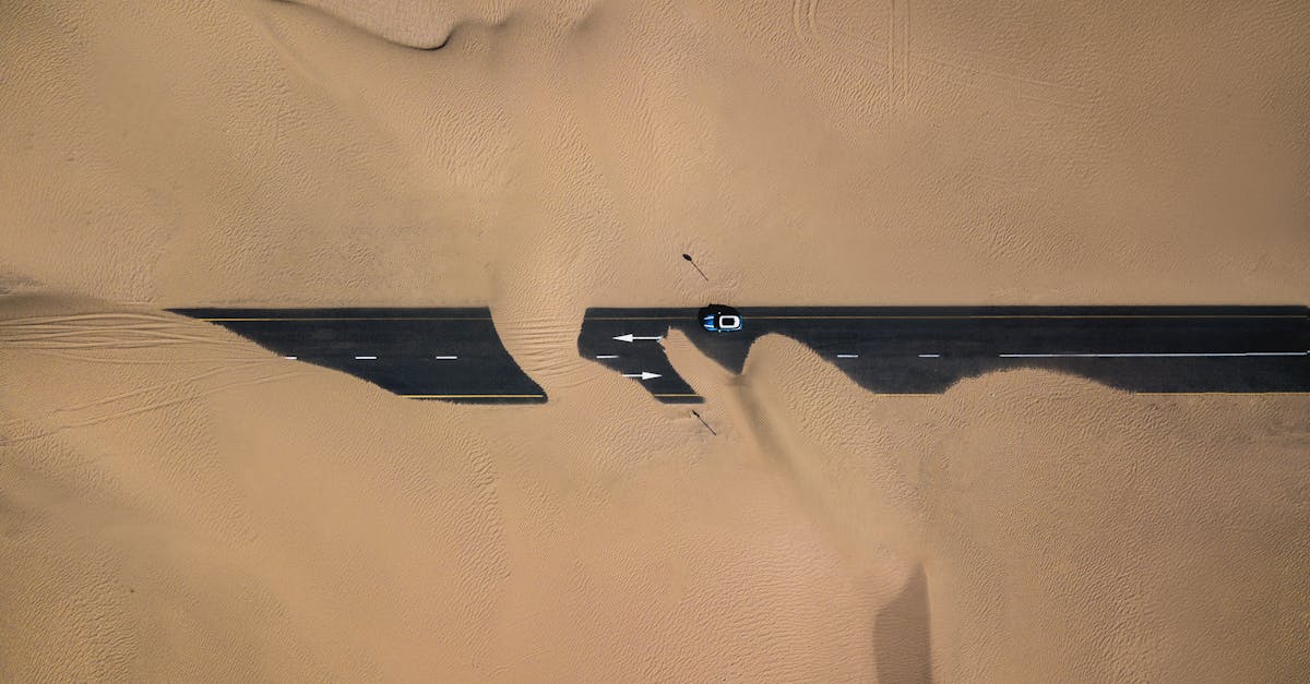 Aerial view of a car on a desert road in Dubai with scenic sand dunes.