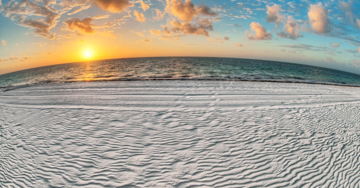 Experience the tranquil beauty of a beach sunrise with golden sun, soft sand, and scattered clouds over the ocean.
