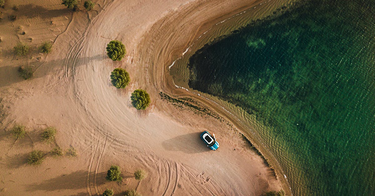 Aerial shot of a sandy beach, water, and parked car in Dubai.