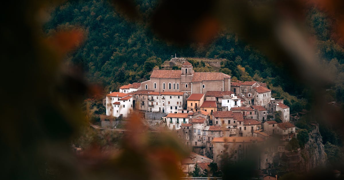 Picturesque view of a rustic Mediterranean village nestled in hills, framed by vibrant autumn foliage.