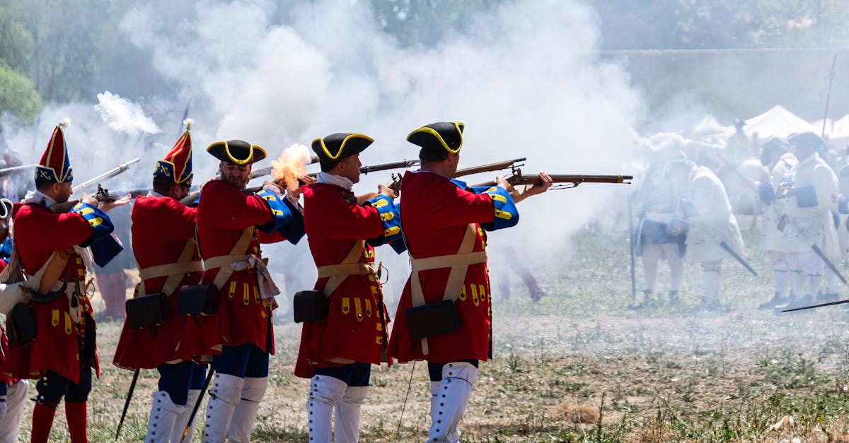 Reenactors in vibrant uniforms firing muskets during a historical battle event.