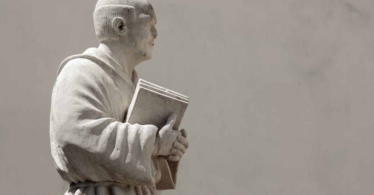 A marble statue of a monk holding a book against a plain background.
