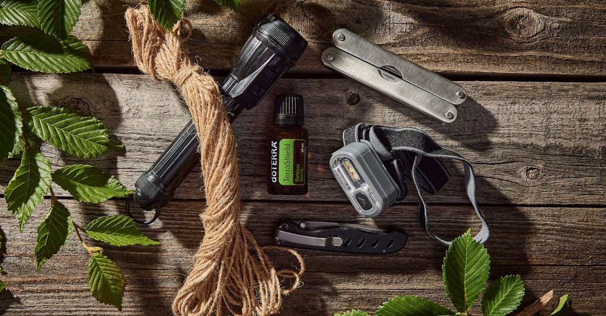 Collection of outdoor essentials including flashlights, rope, pocket knife, and essential oil on a wooden surface.