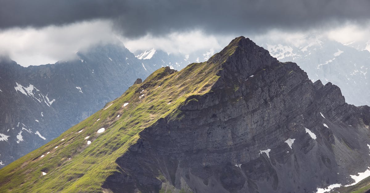 Dramatic mountain landscape with rocky peaks, green slopes, and swirling clouds.