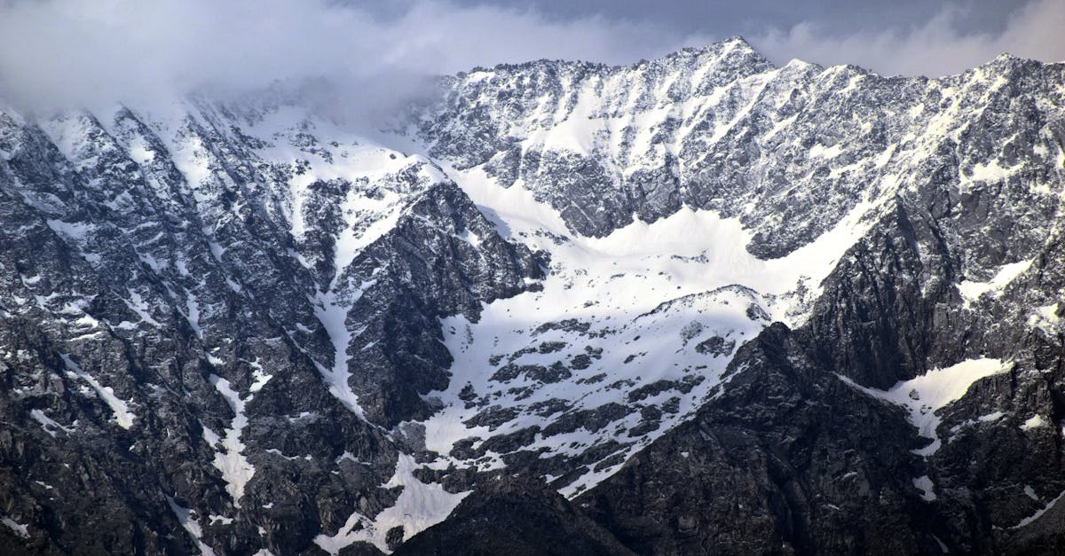 Majestic snow-covered mountain range with rocky peaks under a cloudy sky, ideal for winter travel inspiration.
