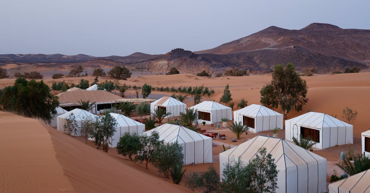 Aerial view of luxury tents in desert landscape with hilly background and twilight ambiance.