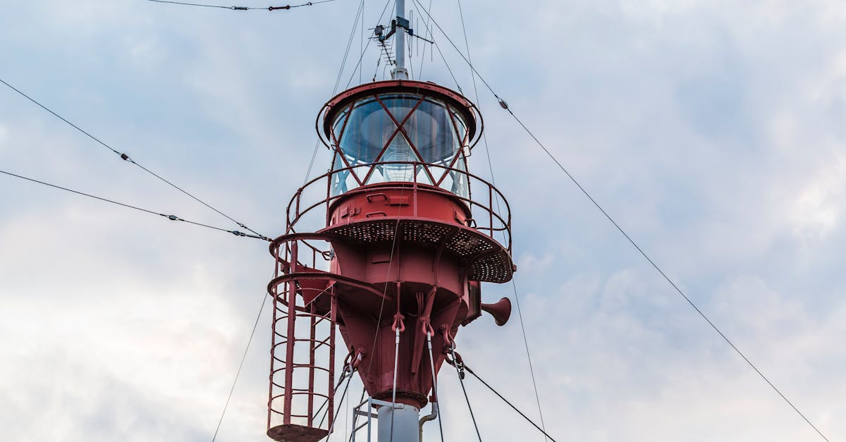 Tall red lighthouse tower with navigation equipment under cloudy skies.