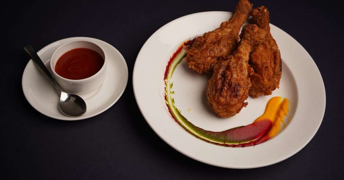 Delicious fried chicken drumsticks served with a side of spicy dipping sauce on a dark background.