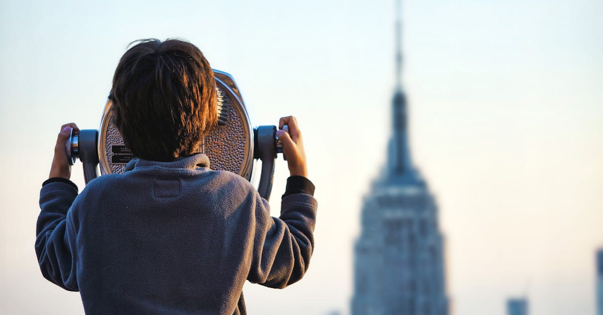 A child uses binoculars to view the Empire State Building in New York City at sunset.