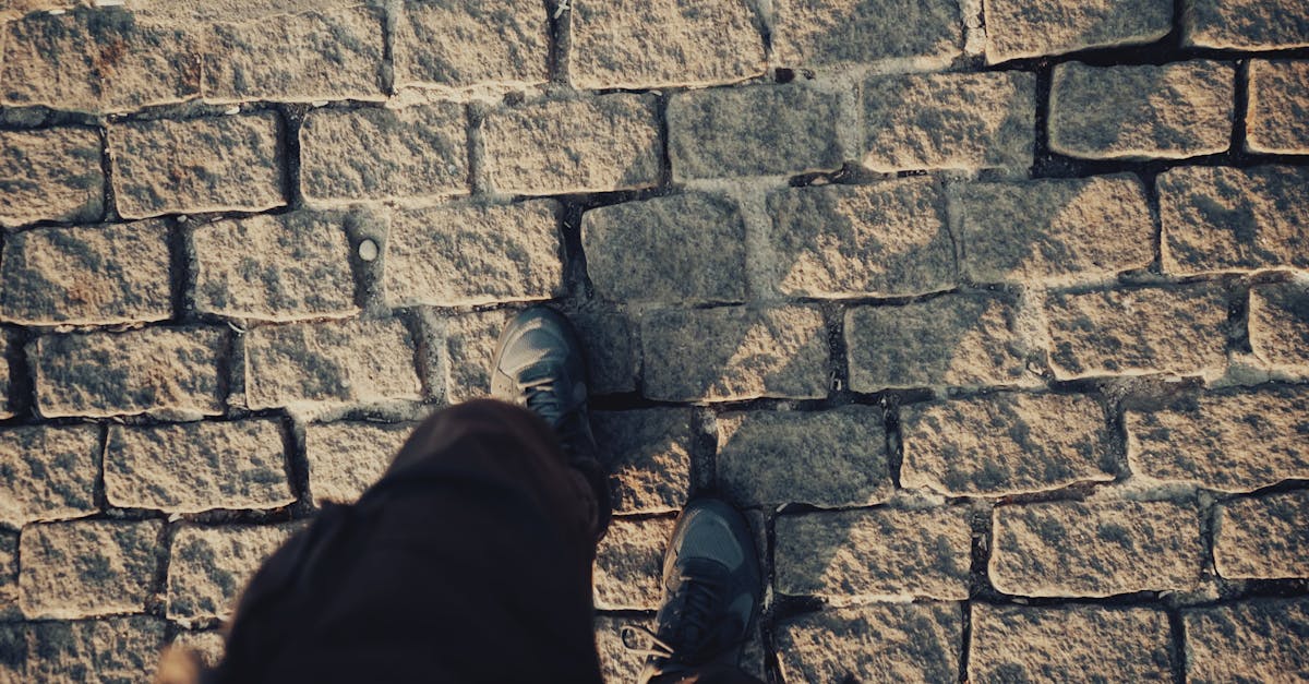 Top view of person walking on a sunlit cobblestone street, casting shadows.