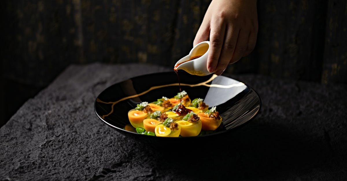 Close-up of a hand pouring sauce onto a gourmet dish in a dark, elegant setting.