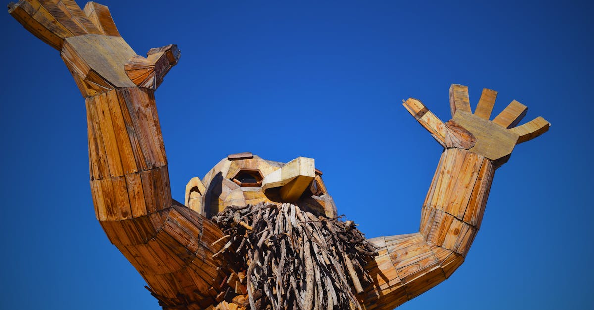 A towering wooden sculpture with arms raised set against a vibrant blue sky, showcasing artistic craftsmanship.