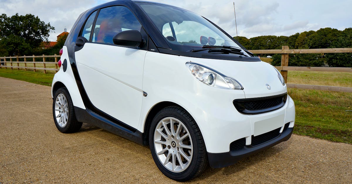 A white Smart Fortwo car parked outdoors with clear sky and greenery.