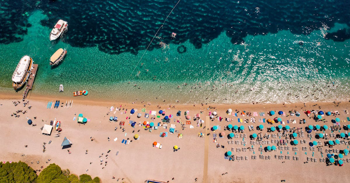 A lively beach scene from above, showcasing colorful umbrellas and clear turquoise water.