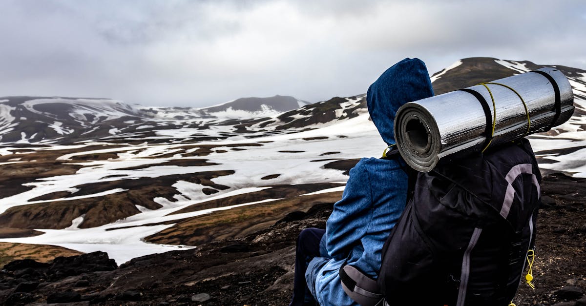 A lone traveler rests with a backpack overlooking the snowy terrain of Iceland's mountains.