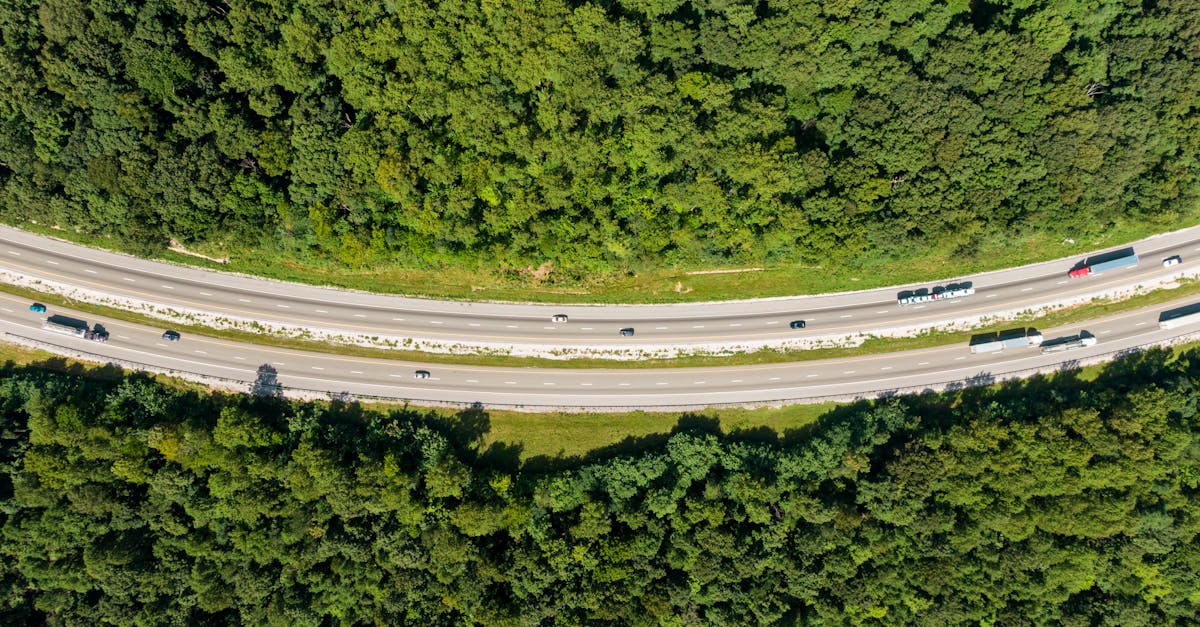 Aerial drone shot of a highway cutting through lush green forest with minimal traffic