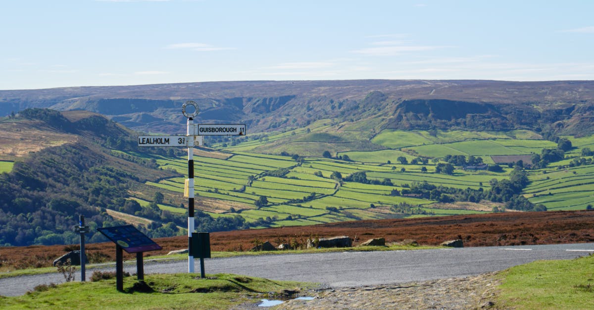Panoramic view of North York Moors with iconic signpost, showcasing lush green landscape on a sunny day.