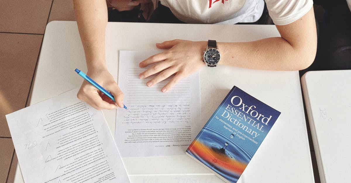 Student writing test using paper and Oxford dictionary on desk in classroom