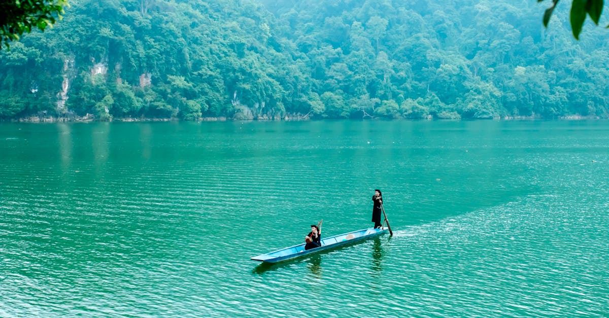 Two people in a boat navigate a tranquil, emerald-colored lake surrounded by lush forest.