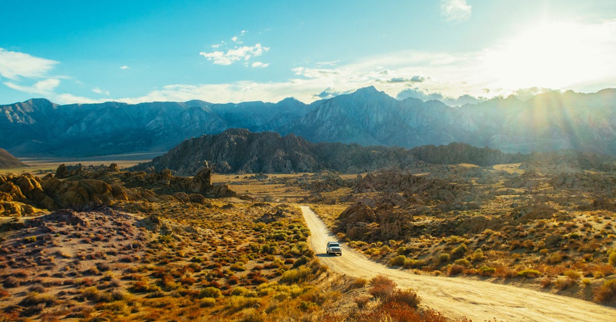 Car driving on a dirt road through a vast mountain landscape at sunset.