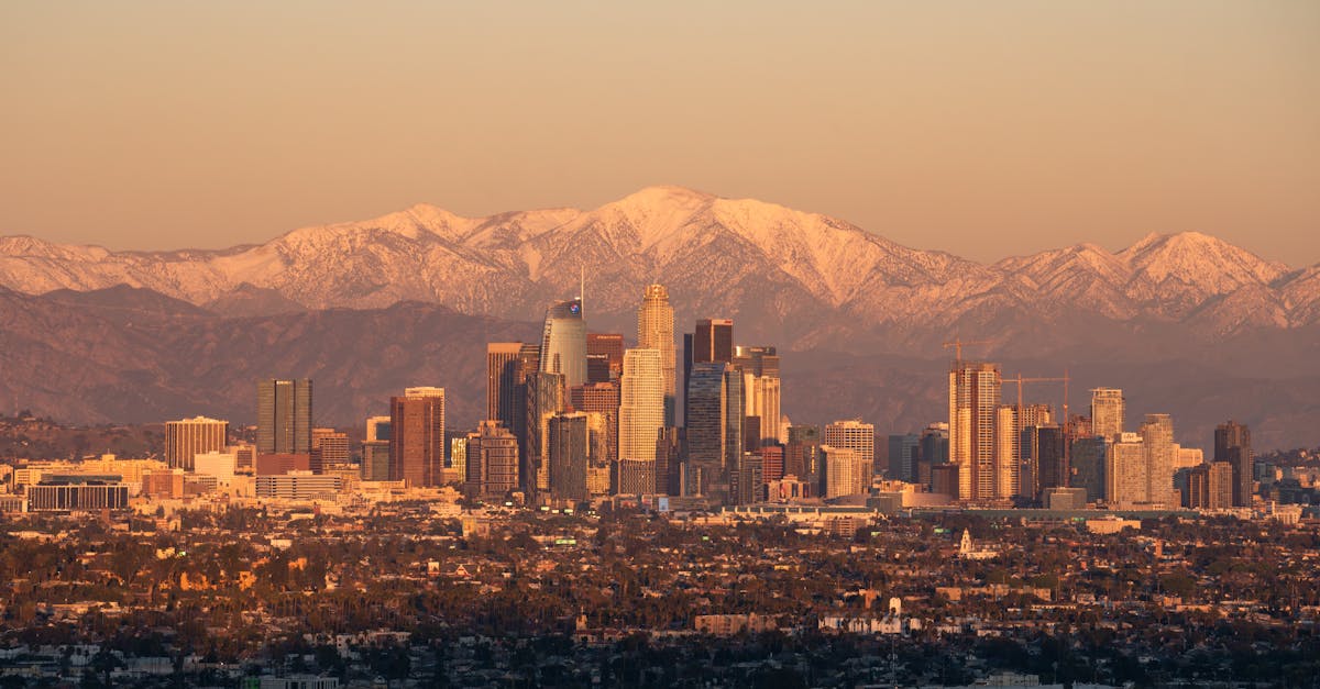 Stunning Los Angeles skyline during golden hour with snow-capped mountains in the background.