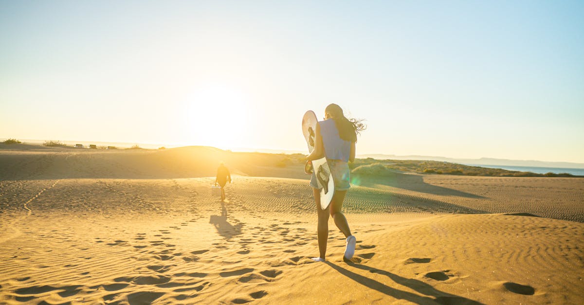 Two people carrying surfboards on a sunny Baja California desert beach at sunset.