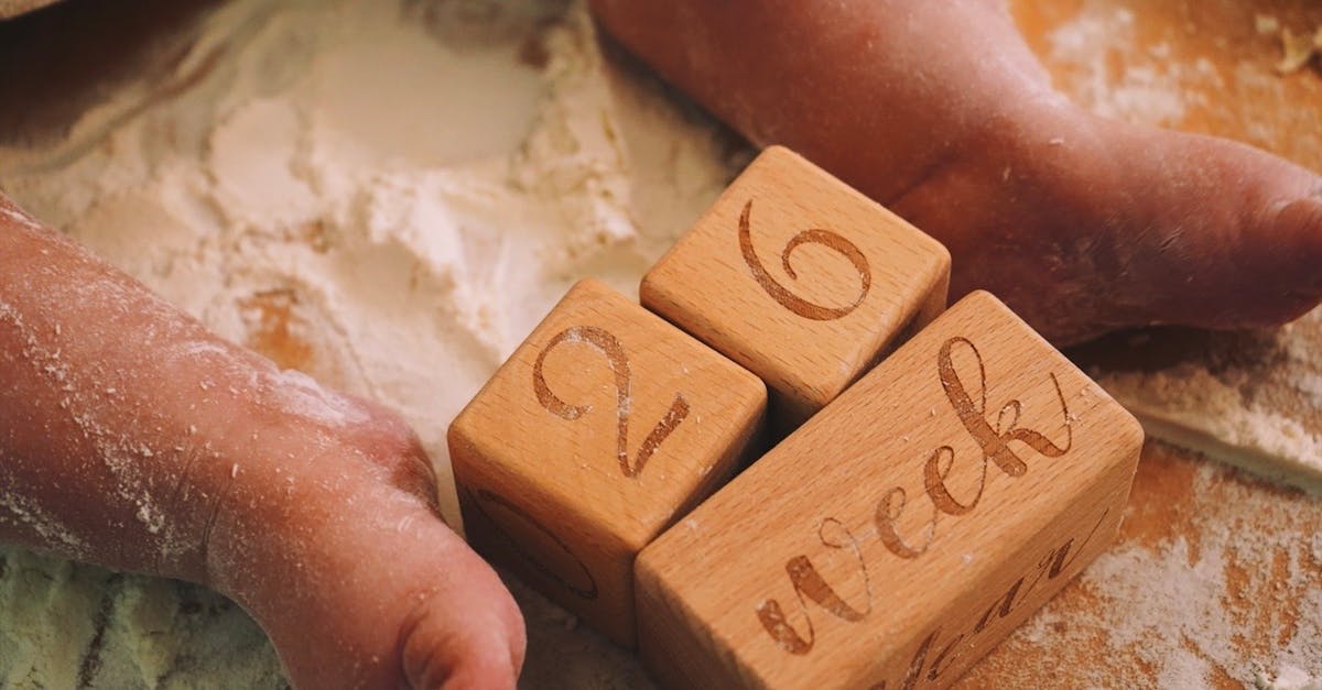 Adorable baby feet on flour-covered surface, next to wooden milestone blocks displaying 26 weeks.