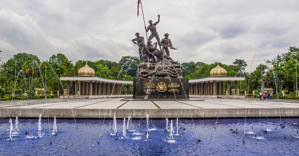 View of the National Monument in Kuala Lumpur, Malaysia, featuring a fountain in the foreground and dramatic clouds.