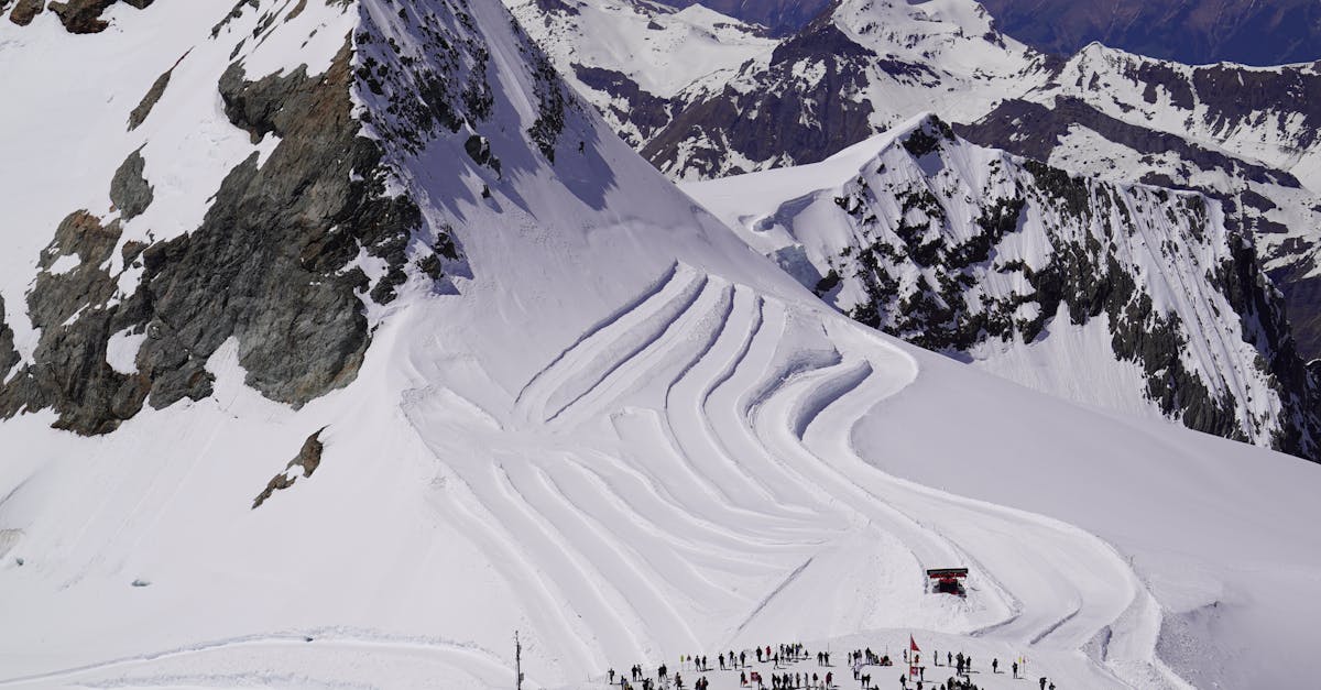Aerial shot of a snowy mountain with skiing trails and a large group gathered at the base.