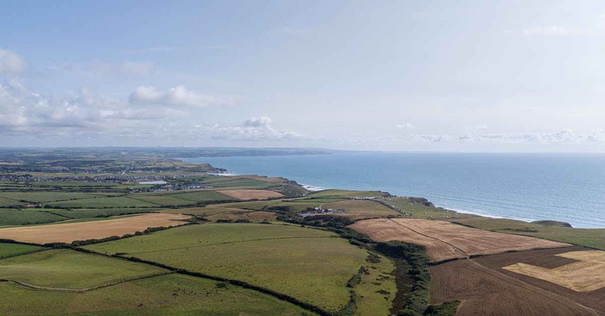 Stunning aerial view of the Cornish coast and patchwork farmlands under a bright sky.