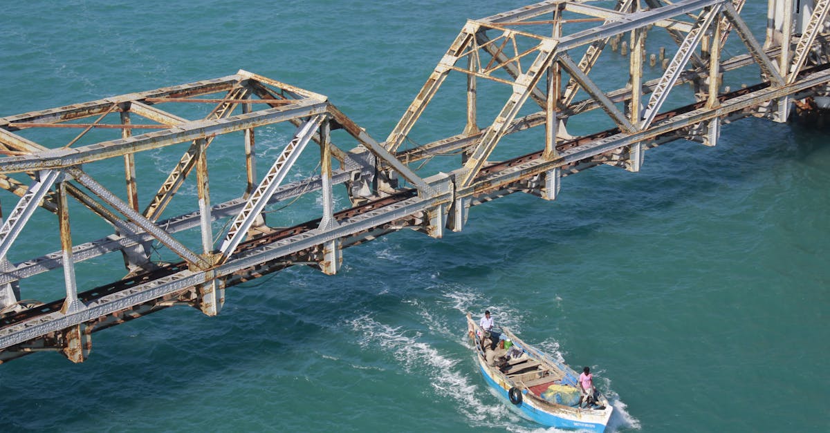 A fishing boat navigates beneath the historic rusty Pamban Bridge in clear blue waters.