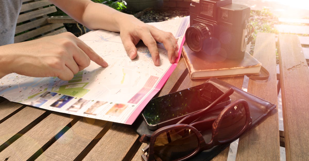 Traveler pointing at map on wooden table with camera and accessories under sunlight.