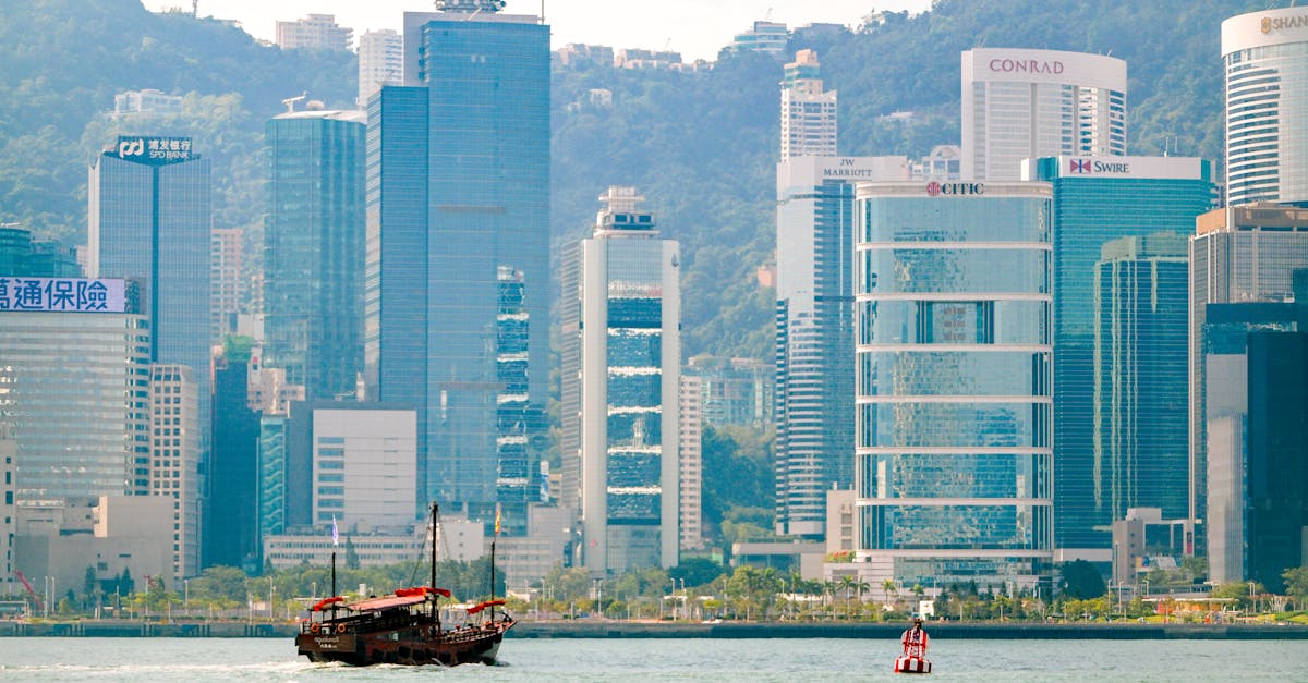 A traditional junk boat sails in front of Hong Kong's iconic skyline, featuring modern skyscrapers.