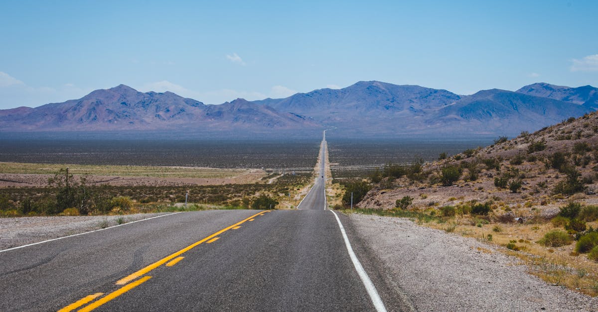 A long straight road stretches through the desert towards distant mountains under a clear blue sky.