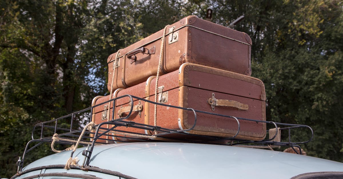Stack of vintage suitcases secured on a classic car roof rack for an outdoor road trip.