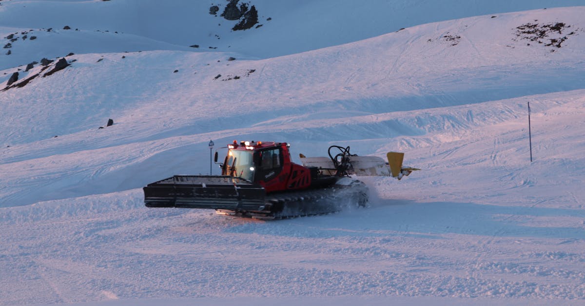 A snow grooming machine prepares a ski slope during a picturesque sunset in winter mountains.