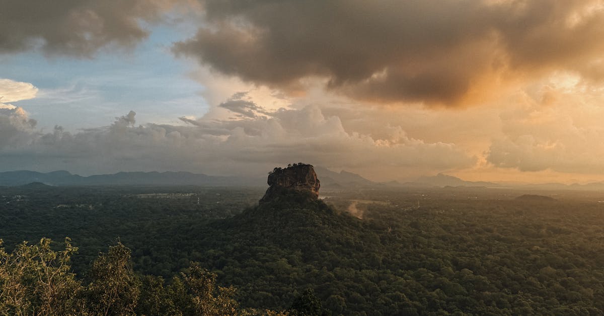 Sigiriya Rock Fortress surrounded by lush greenery under a dramatic sunset sky in Sri Lanka.