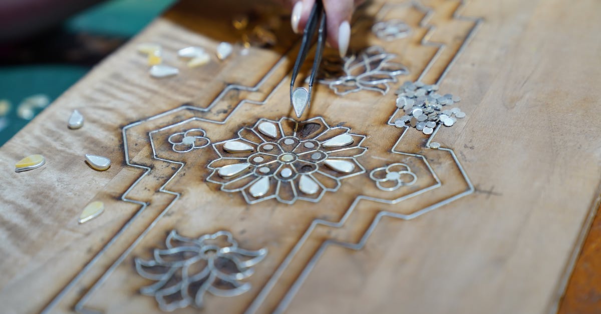 Close-up of a craftsman using tweezers to create detailed wood inlay with floral patterns.