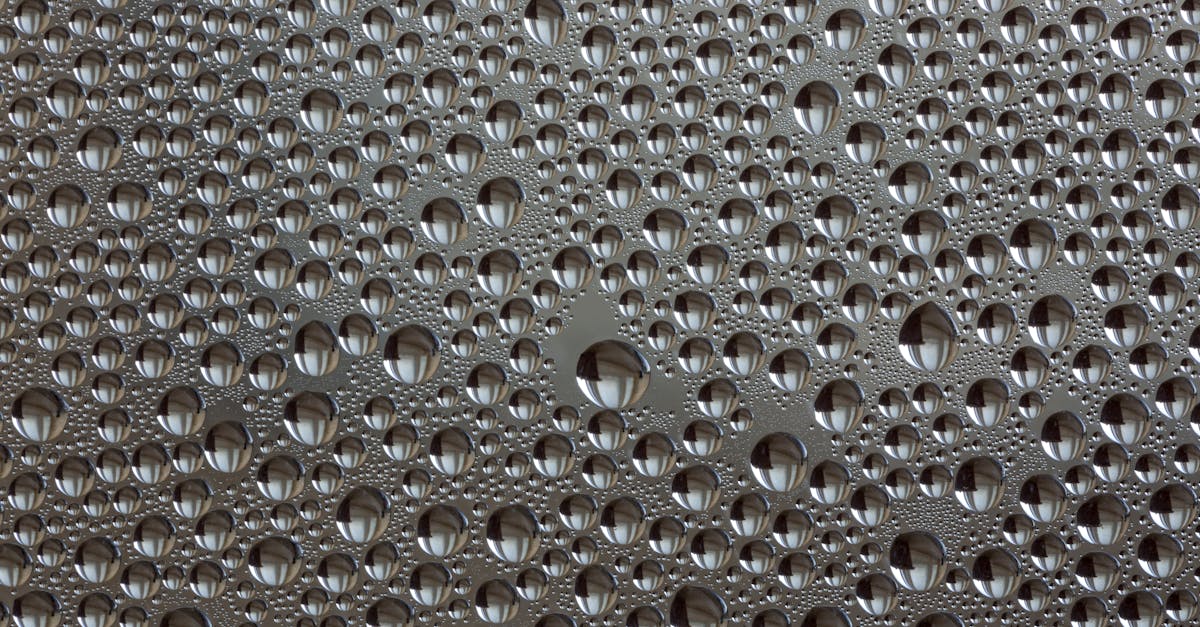 Close-up of water droplets forming abstract patterns on a metallic surface, showcasing reflection and texture.