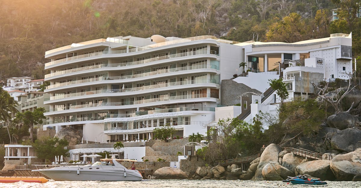 A luxurious resort building on a scenic coastal hillside at sunset, featuring yachts in the foreground.
