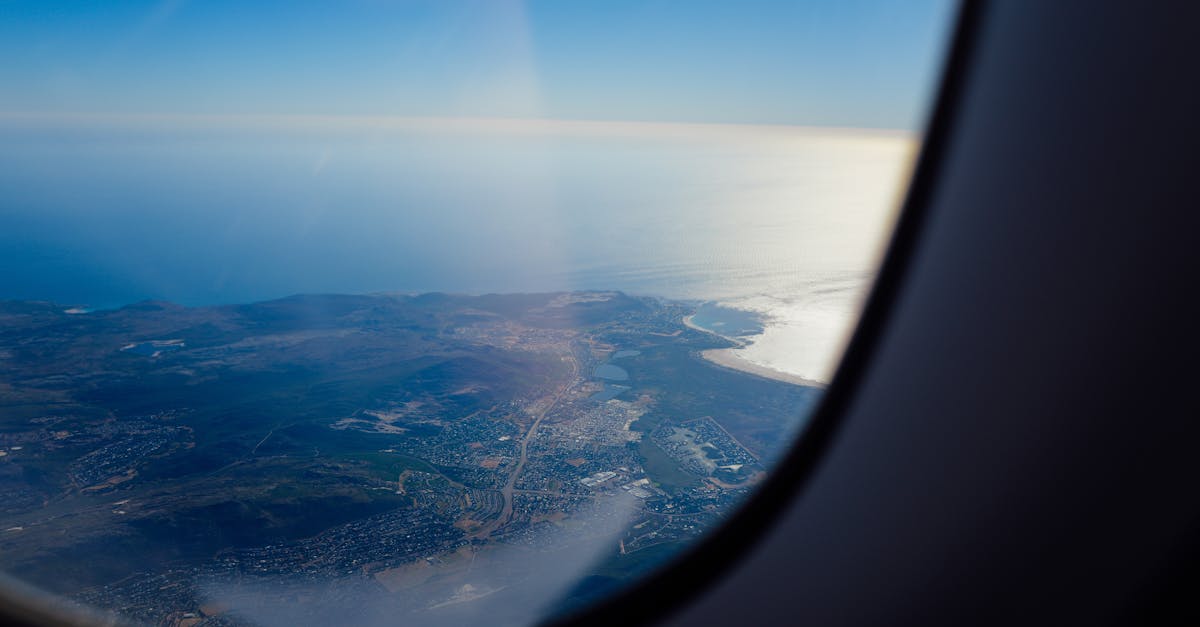 Stunning aerial view of coastline through airplane window at daytime, capturing land and sea merging.
